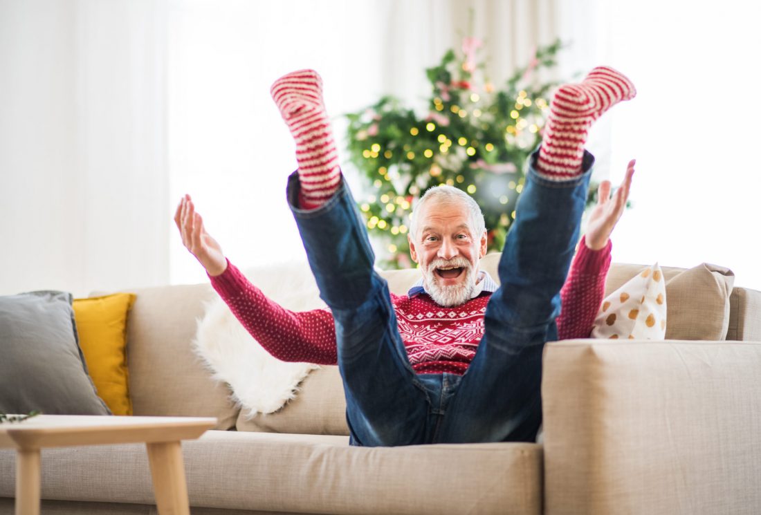 A cheerful senior man with striped red and white socks at home at Christmas time sitting on a sofa, having fun.