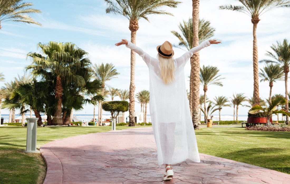 Back view of happy excited young woman with raised hands walking and enjoying on summer resort