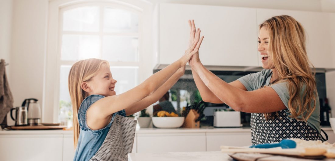 Little girl and her mother in kitchen giving high five