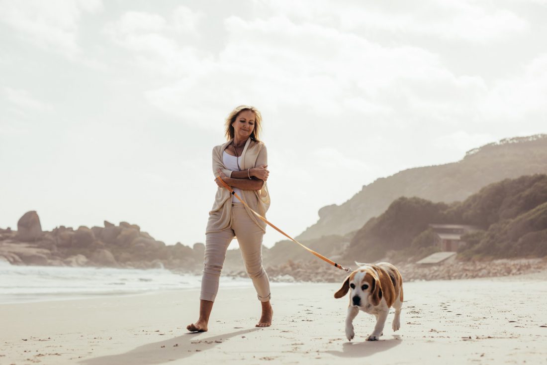 Mature-Woman-Walking-Her-Dog-on-the-Beach.jpg